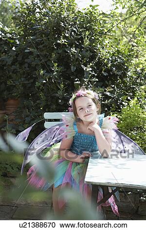 Portrait of young girl (5-6) in fairy costume sitting at garden table View Large Photo Image Stock Image - Portrait of young girl (5-6) in fairy costume sitting at garden table. Fotosearch