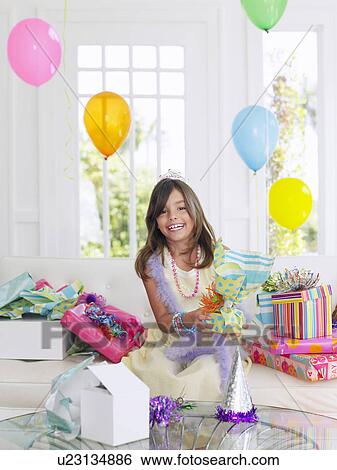Stock Photograph - Portrait of young girl (7-9) with birthday presents smiling. Fotosearch
