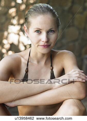 Stock Image - Portrait of young woman in bikini sitting with arms crossed. Fotosearch