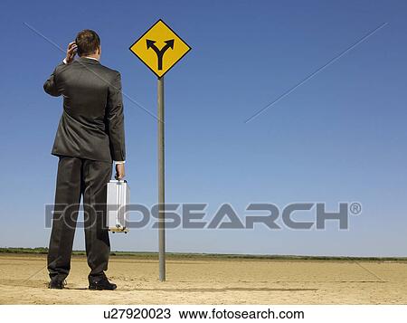 Rear view of confused businessman looking at desert road sign View Large Photo Image Stock Image - Rear view of confused businessman looking at desert road sign. Fotosearch