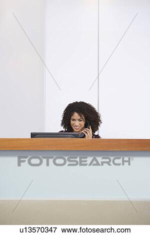 Receptionist sitting behind reception desk talking on Telephone View Large Photo Image Stock Photo - Receptionist sitting behind reception desk talking on Telephone. Fotosearch