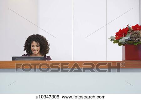 Receptionist sitting behind reception desk Using computer View Large Photo Image Stock Photograph - Receptionist sitting behind reception desk Using computer. Fotosearch