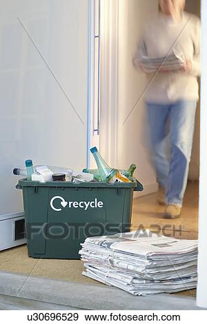 Stock Photo - Recycling container and pile of waste paper on floor woman walking in background (motion blur). Fotosearch