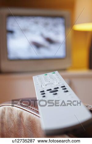Remote control lying on armchair with television turned on in background close-up View Large Photo Image Stock Photo - Remote control lying on armchair with television turned on in background close-up. Fotosearch