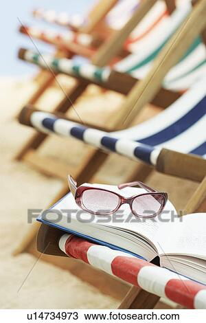 Stock Image - Row of deck chairs on beach book with sunglasses in foreground. Fotosearch