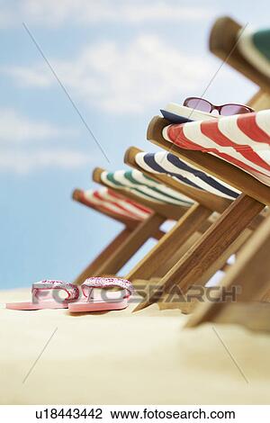 Row of deck chairs on beach focus on flip-flops on ground View Large Photo Image Stock Image - Row of deck chairs on beach focus on flip-flops on ground. Fotosearch
