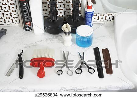 Picture - Scissors combs razor brush and hair products on counter in barber shop. Fotosearch