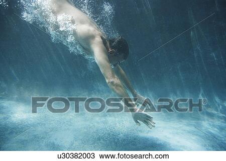 Stock Image - Semi-dressed man swimming side view underwater view. Fotosearch