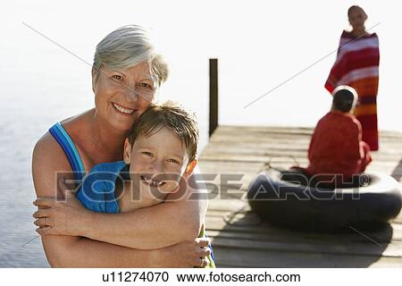 Senior woman hugging grandson (5-6) on dock with two children (7-9) in background. View Large Photo Image Stock Image - Senior woman hugging grandson (5-6) on dock with two children (7-9) in background.. Fotosearch