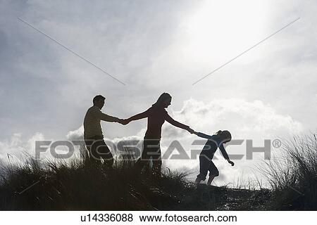 Stock Photo - Silhouette of parents and daughter (5-6) holding hands on sand dunes. Fotosearch