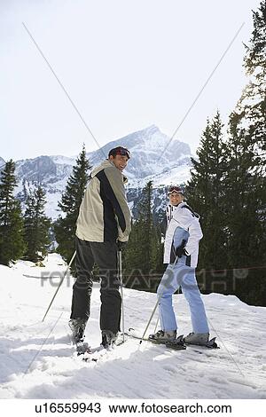 Stock Image - Skiing couple looking over shoulder standing on ski slope back view. Fotosearch