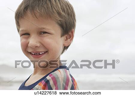 Stock Photo - Smiling boy (5-6) on beach portrait. Fotosearch