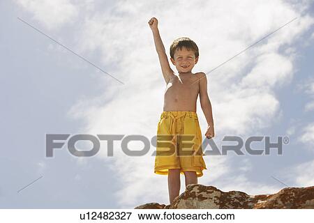 Smiling boy (5-6) standing on rock on beach low angle view View Large Photo Image Stock Photo - Smiling boy (5-6) standing on rock on beach low angle view. Fotosearch