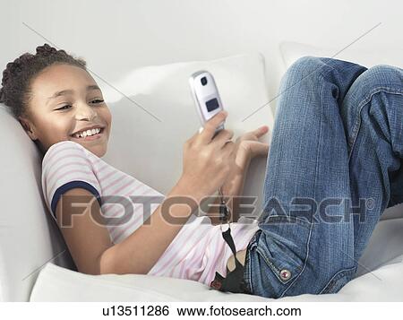 Stock Photograph - Smiling Girl lying on sofa using Cell Phone side view. Fotosearch
