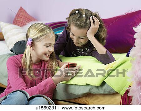 Smiling girls in bedroom looking at mobile phone View Large Photo Image Stock Image - Smiling girls in bedroom looking at mobile phone. Fotosearch