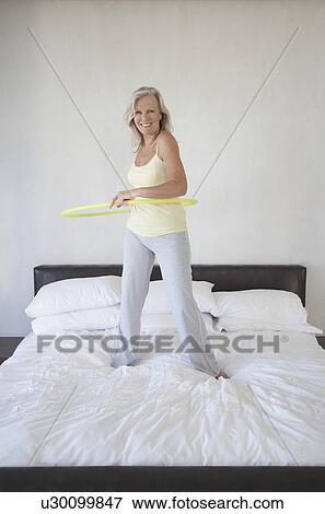 Smiling Mature woman standing on bed holding hula hoop View Large Photo Image Stock Photo - Smiling Mature woman standing on bed holding hula hoop. Fotosearch