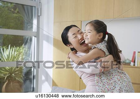 Stock Photo - Smiling Woman Hugging her Daughter in living room. Fotosearch