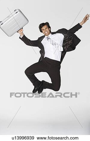 Smiling young businessman holding briefcase jumping clicking heels View Large Photo Image Stock Photo - Smiling young businessman holding briefcase jumping clicking heels. Fotosearch
