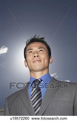 Stock Image - Smiling Young Businessman standing outside low angle view. Fotosearch