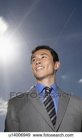 Stock Photo - Smiling Young Businessman standing outside low angle view. Fotosearch