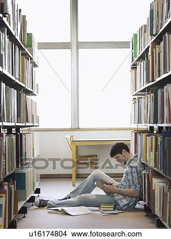 Picture - Student reading sitting on floor in library. Fotosearch