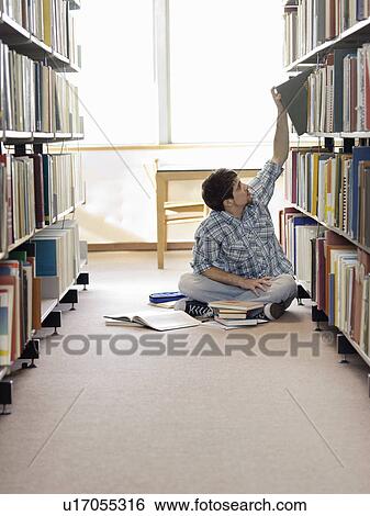 Student sitting on floor in library reaching for book View Large Photo Image Stock Photograph - Student sitting on floor in library reaching for book. Fotosearch