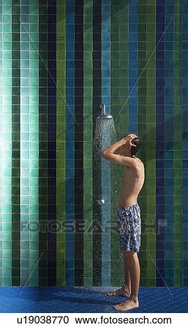 Stock Image - Teenage boy (16-17) standing under outdoor shower side view. Fotosearch