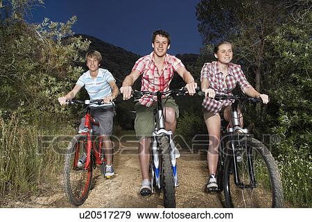 Stock Photo - Teenage boys and girl (16-17 years) riding bikes on country road in evening. Fotosearch
