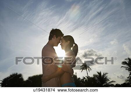 Picture - Teenage couple (16-17) embracing on beach at sunset side view. Fotosearch