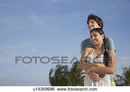 Stock Photograph - Teenage couple (16-17) embracing on beach. Fotosearch