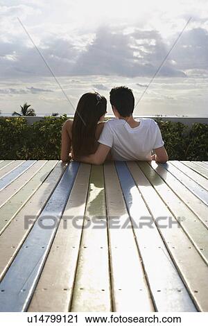 Teenage couple (16-17) sitting on wooden deck looking at view back view View Large Photo Image Stock Image - Teenage couple (16-17) sitting on wooden deck looking at view back view. Fotosearch