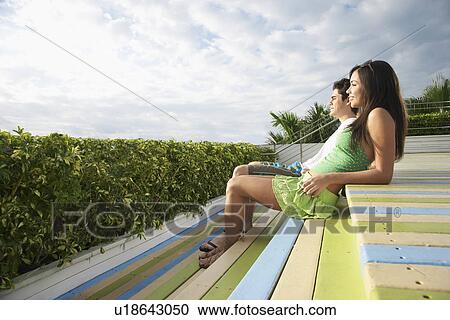 Teenage couple (16-17) sitting on wooden deck looking at view side view View Large Photo Image Stock Image - Teenage couple (16-17) sitting on wooden deck looking at view side view. Fotosearch