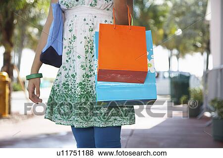 Teenage girl (16-17) carrying shopping bags walking on street mid section View Large Photo Image Stock Photo - Teenage girl (16-17) carrying shopping bags walking on street mid section. Fotosearch