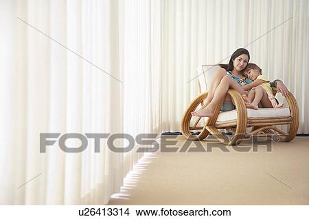 Picture - Teenage girl (16-18) sitting on armchair with sister (5-6). Fotosearch