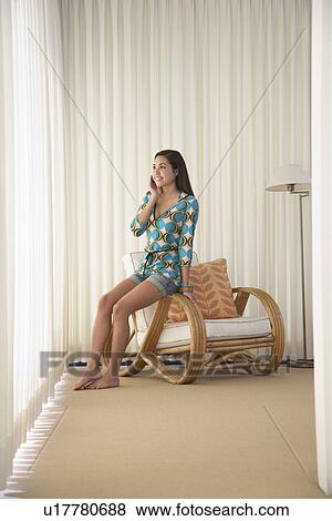 Stock Photo - Teenage girl (16-18) sitting on armchair talking on mobile phone. Fotosearch