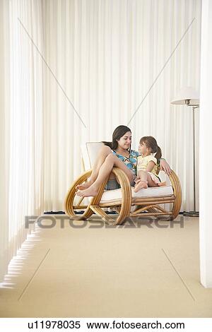 Stock Photography - Teenage girl (16-18) sitting on armchair with sister (5-6). Fotosearch