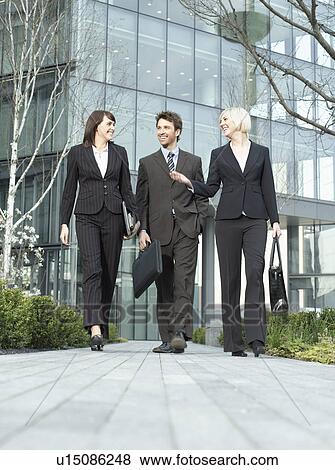 Three business people walking outside office building talking and smiling (surface view) View Large Photo Image Stock Photo - Three business people walking outside office building talking and smiling (surface view). Fotosearch