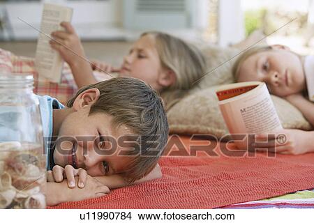 Picture - Three children (5-6 7-910-12) lying on blanket outdoors focus on boy. Fotosearch