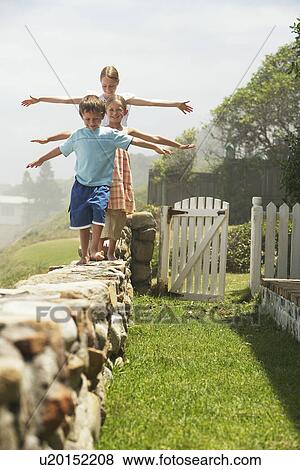 Stock Photo - Three children (5-6 7-910-12) walking in row on stone wall. Fotosearch