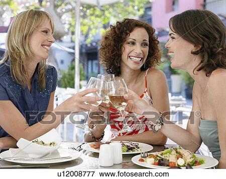 Stock Photo - Three female friends toasting drinks at outdoor cafe. Fotosearch