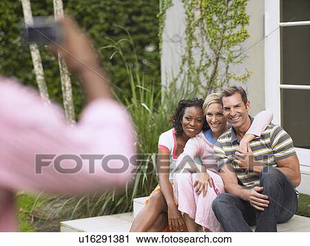 Stock Image - Three friends being photographed outdoors. Fotosearch