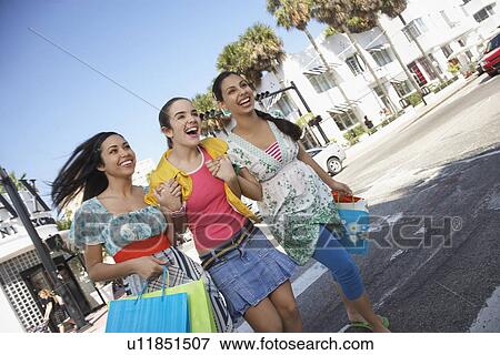 Stock Photo - Three teenage girls (16-17) carrying shopping bags crossing street. Fotosearch