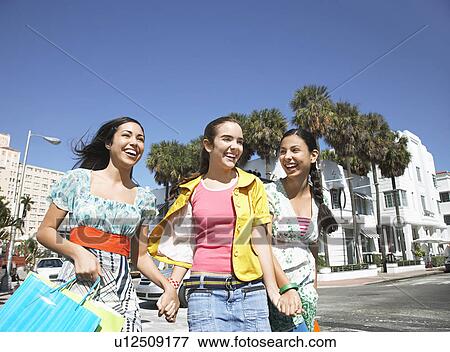 Stock Photo - Three teenage girls (16-17) carrying shopping bags walking on street. Fotosearch