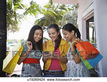 Picture - Three teenage girls (16-17) on street holding shopping bags and text messaging. Fotosearch