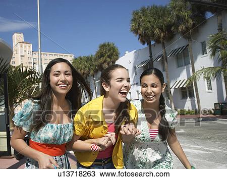 Stock Image - Three teenage girls (16-17) walking on street and laughing. Fotosearch
