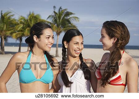 Stock Image - Three teenage girls (16-17) wearing bikinis standing on beach portrait. Fotosearch