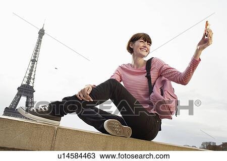 Stock Image - Tourist Using Camera Phone and Eiffel Tower. Fotosearch