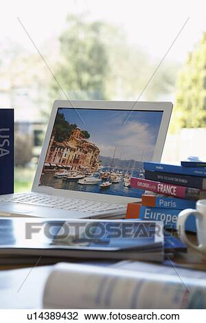 Stock Image - Travel guides next to laptop on table. Fotosearch