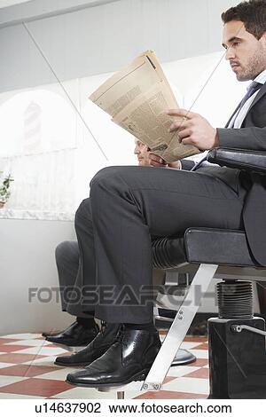 Stock Image - Two business men waiting for haircut in barber shop. Fotosearch