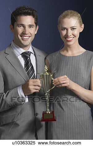 Two business people holding trophy against dark background View Large Photo Image Stock Photography - Two business people holding trophy against dark background. Fotosearch
